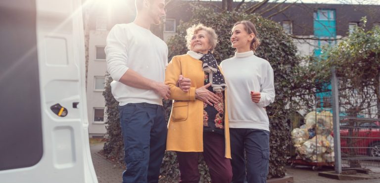 man and woman carer helping elderly lady into non-emergency medical transportation