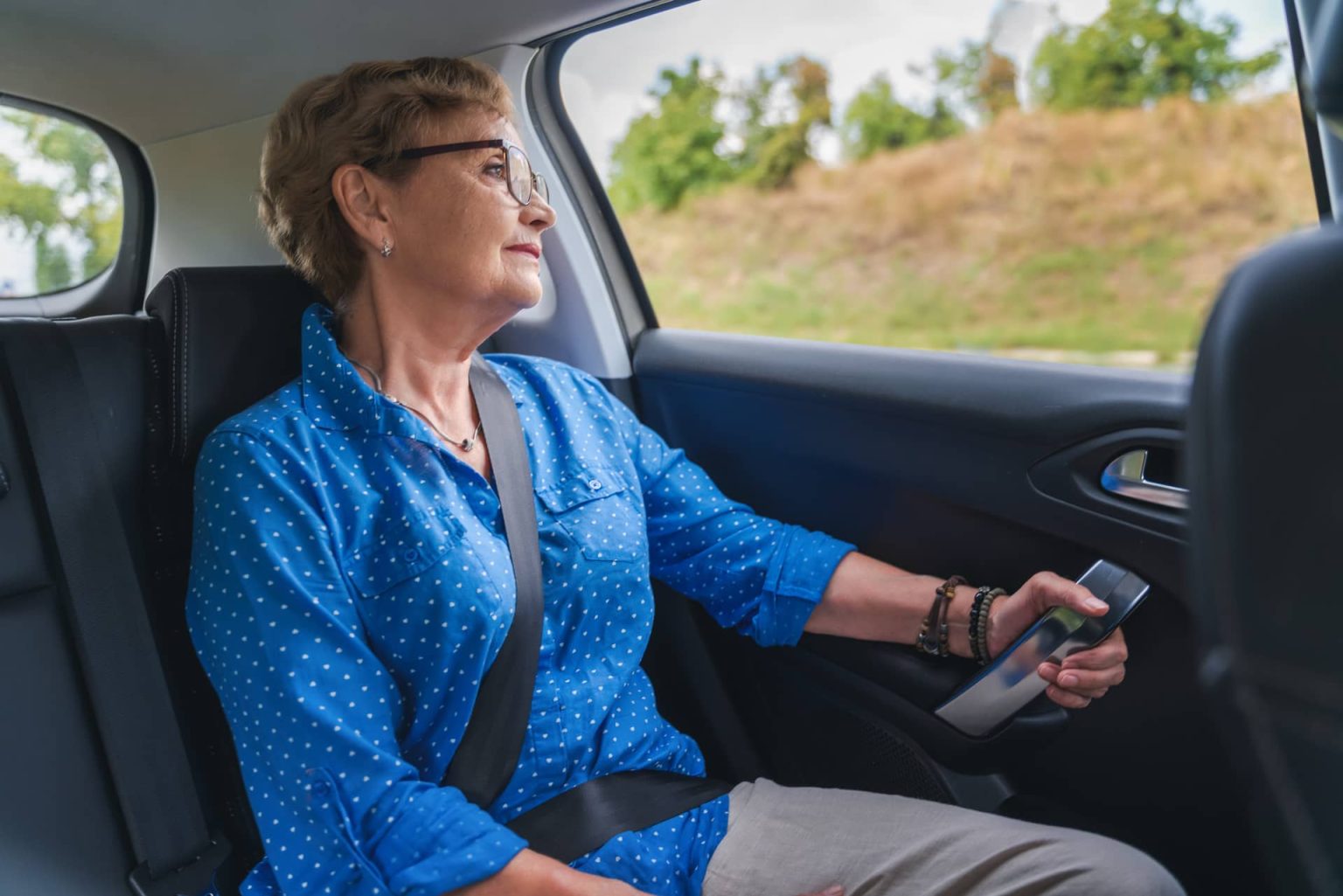 An elderly woman is sitting in the back seat of a car.