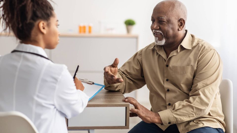 Consultancy A black man talking to a doctor in a doctor's office.