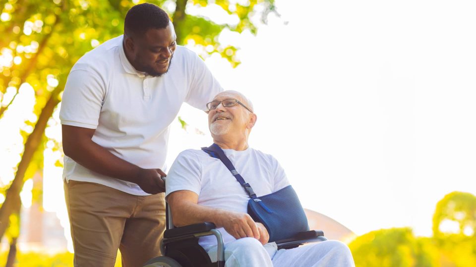 Wellness banner 2 A man in a wheelchair is being helped by another man in a wheelchair.